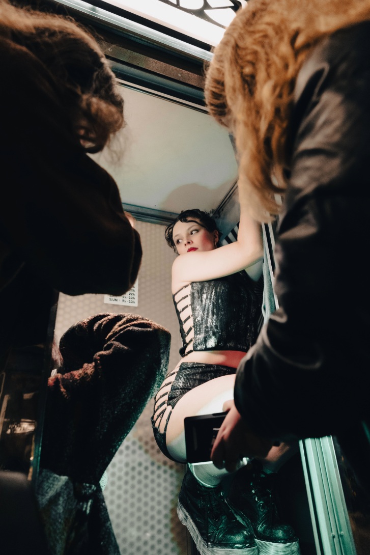 La mannequin posant dans une cabine, entourée de l’équipe de tournage, pour illustrer la singularité de la collection Mak Lingerie.