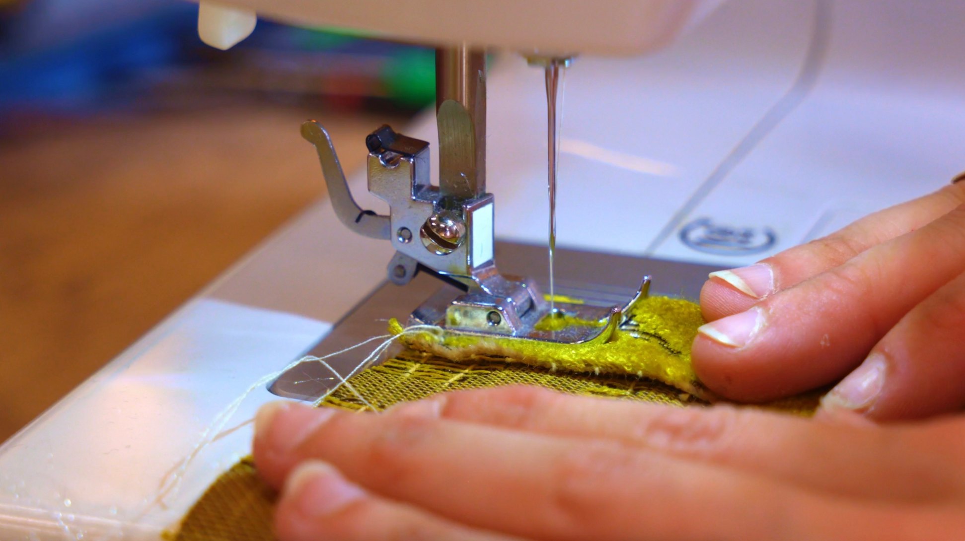 Plan rapproché montrant une main guidant du tissu sous une machine à coudre pour la fabrication artisanale d’un accessoire Broc'n'Roll.