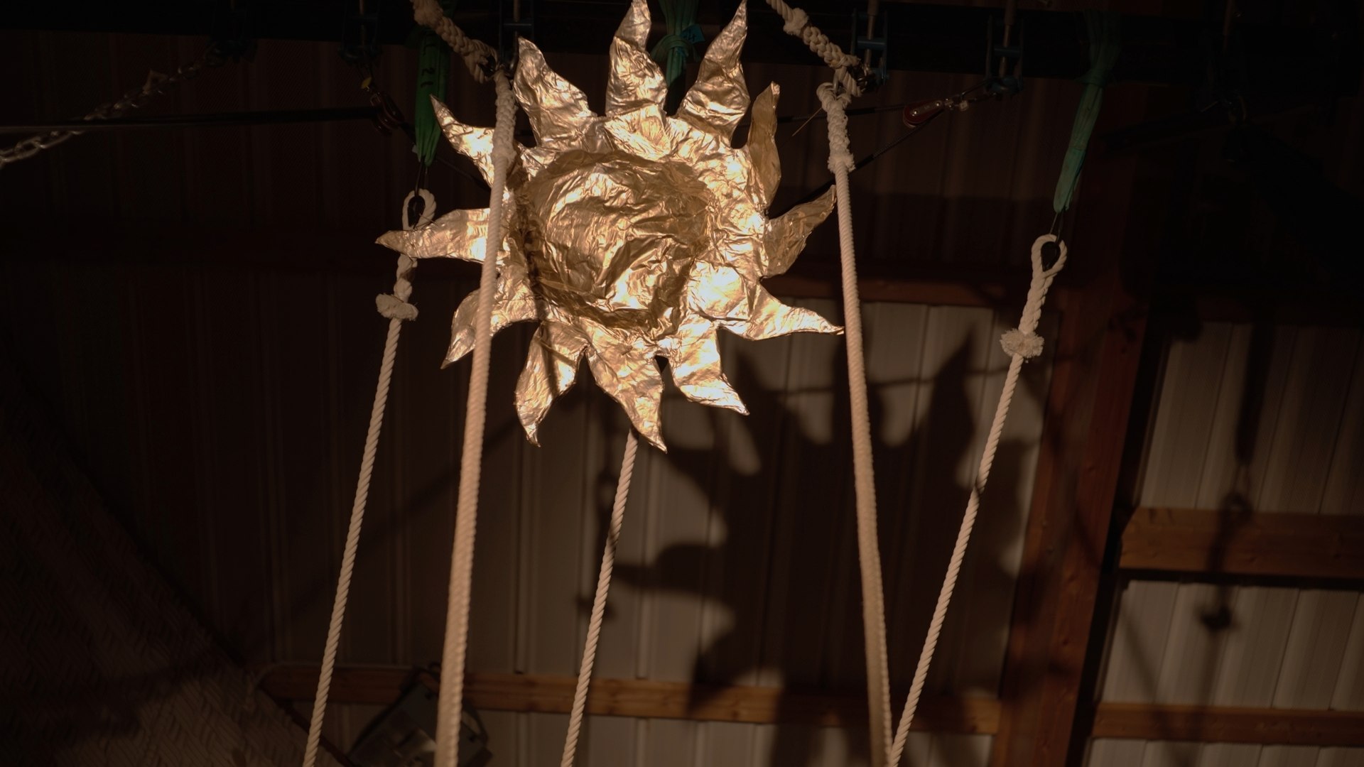 Décor doré en forme de soleil suspendu par des cordes dans un espace scénique du projet Icare, réalisé par O3il Production.