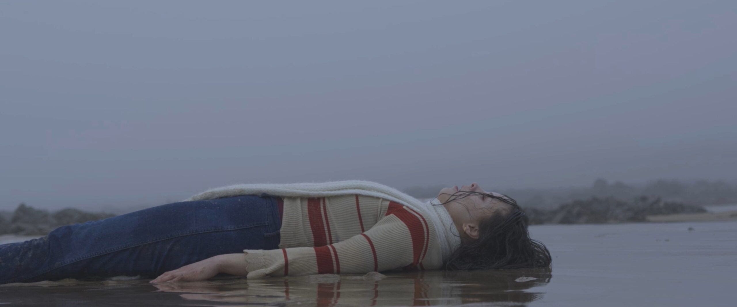 Femme étendue sur le sable dans une scène poignante du court-métrage Entre Deux Eaux.