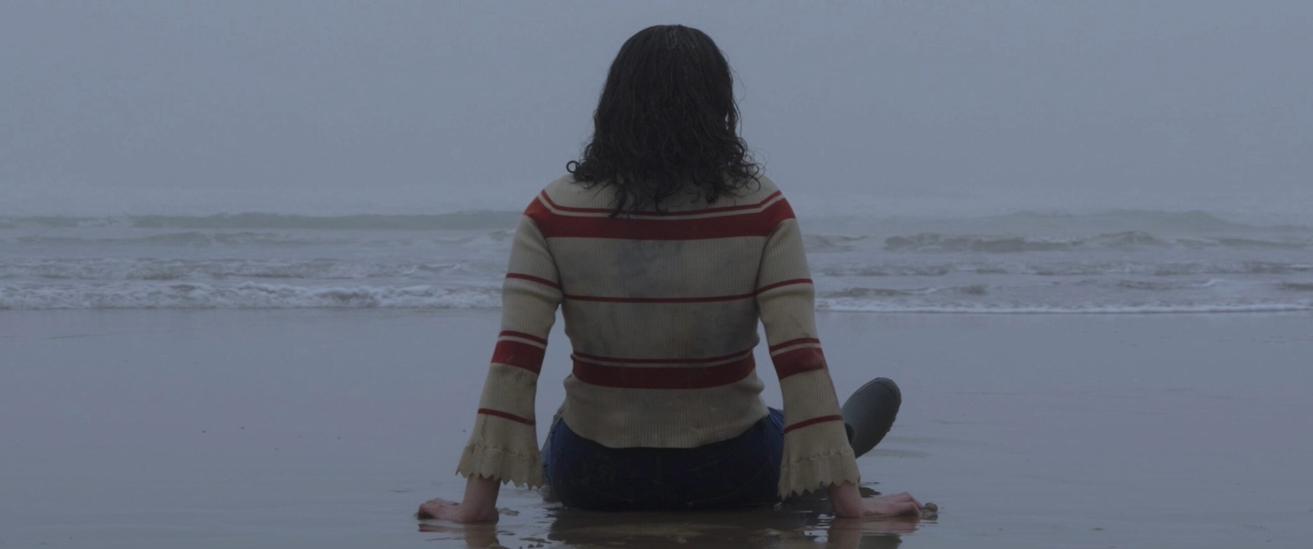 Femme assise face à l’océan dans une atmosphère sombre et brumeuse, scène finale de Entre Deux Eaux.