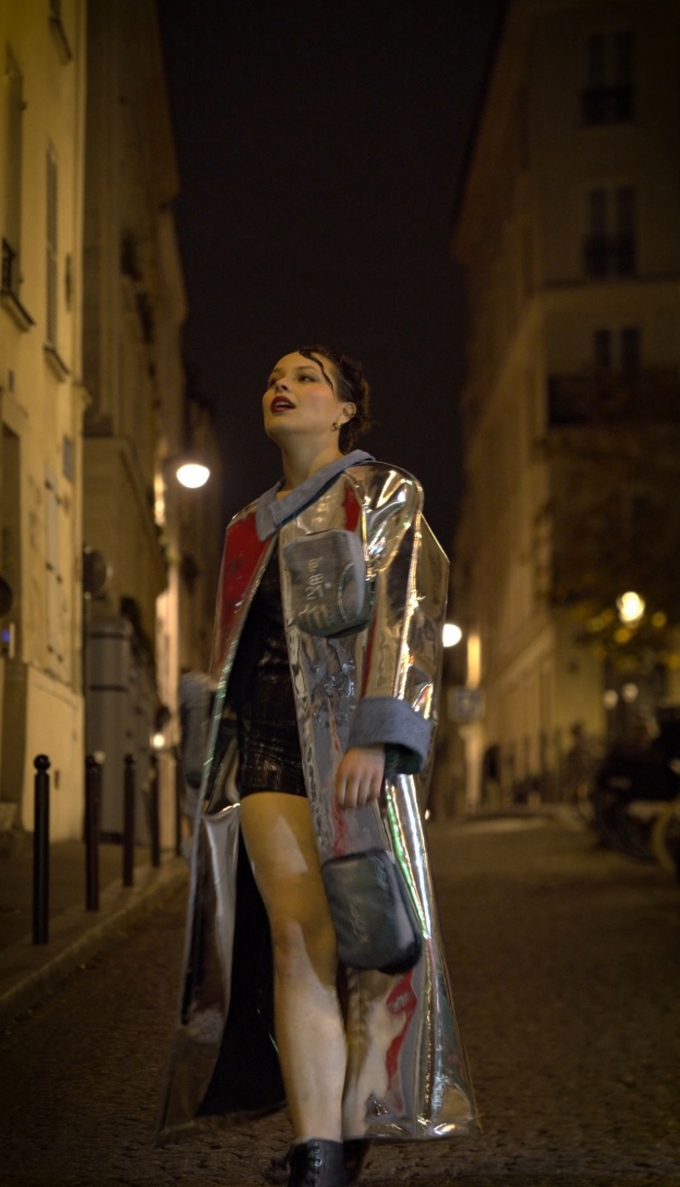 Femme en manteau chromé déambulant dans une rue parisienne de nuit, incarnant l’élégance contemporaine de Mak Lingerie.