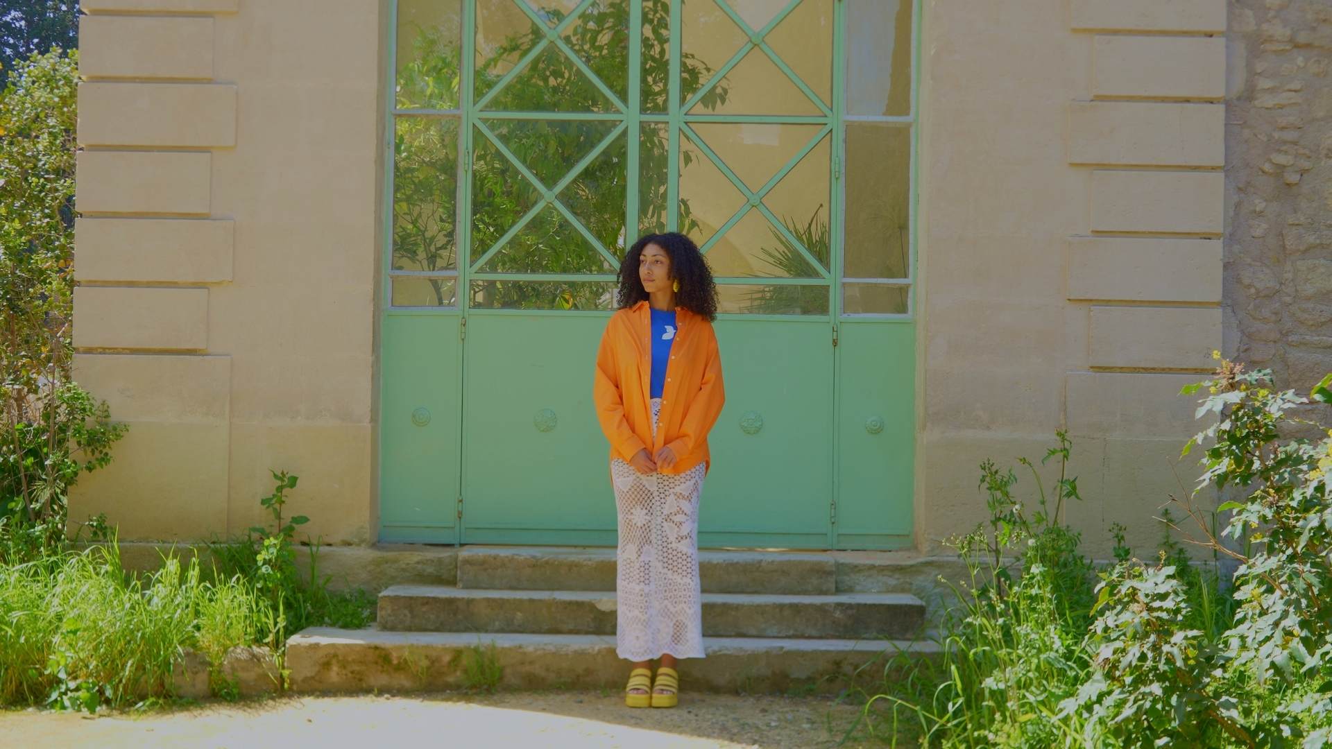 Modèle portant une tenue colorée Maison Janie, posant devant une grande porte verte, projet mode éthique capté par O3il Production.