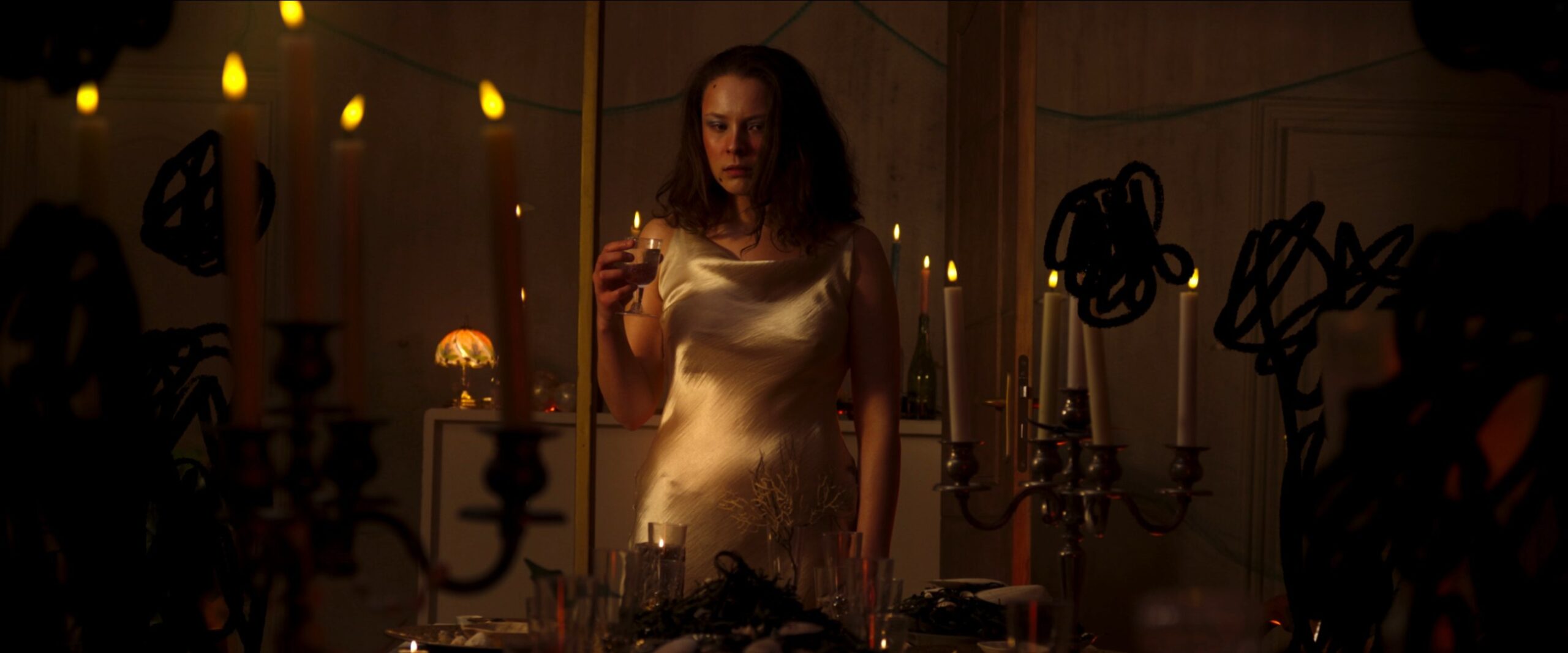 Isalys, personnage principal du court-métrage Entre deux eaux, se tient dans une pièce sombre éclairée par des bougies, dans une ambiance onirique et mystérieuse.