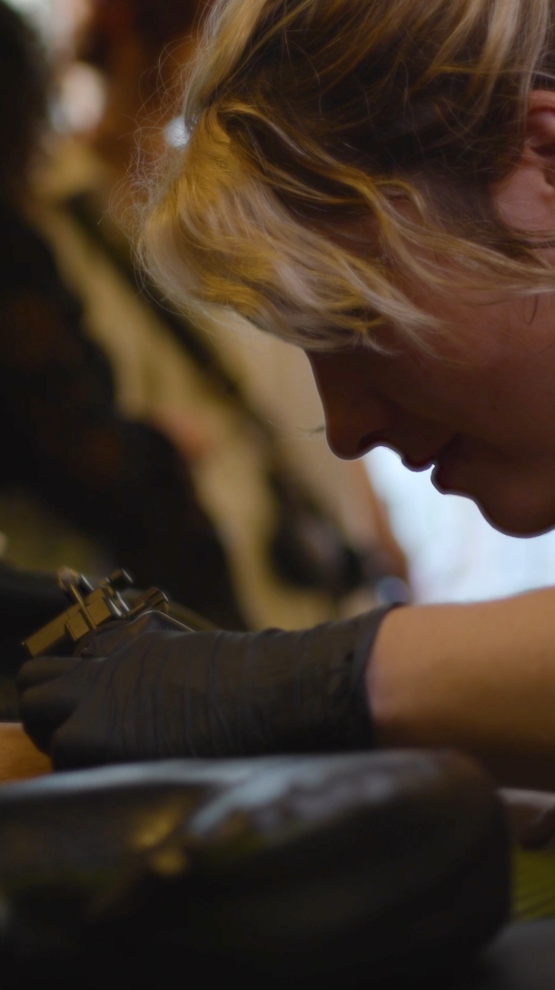 Vue rapprochée d’une tatoueuse concentrée, machine à la main, pendant le flashday organisé par Vanitheuse.
