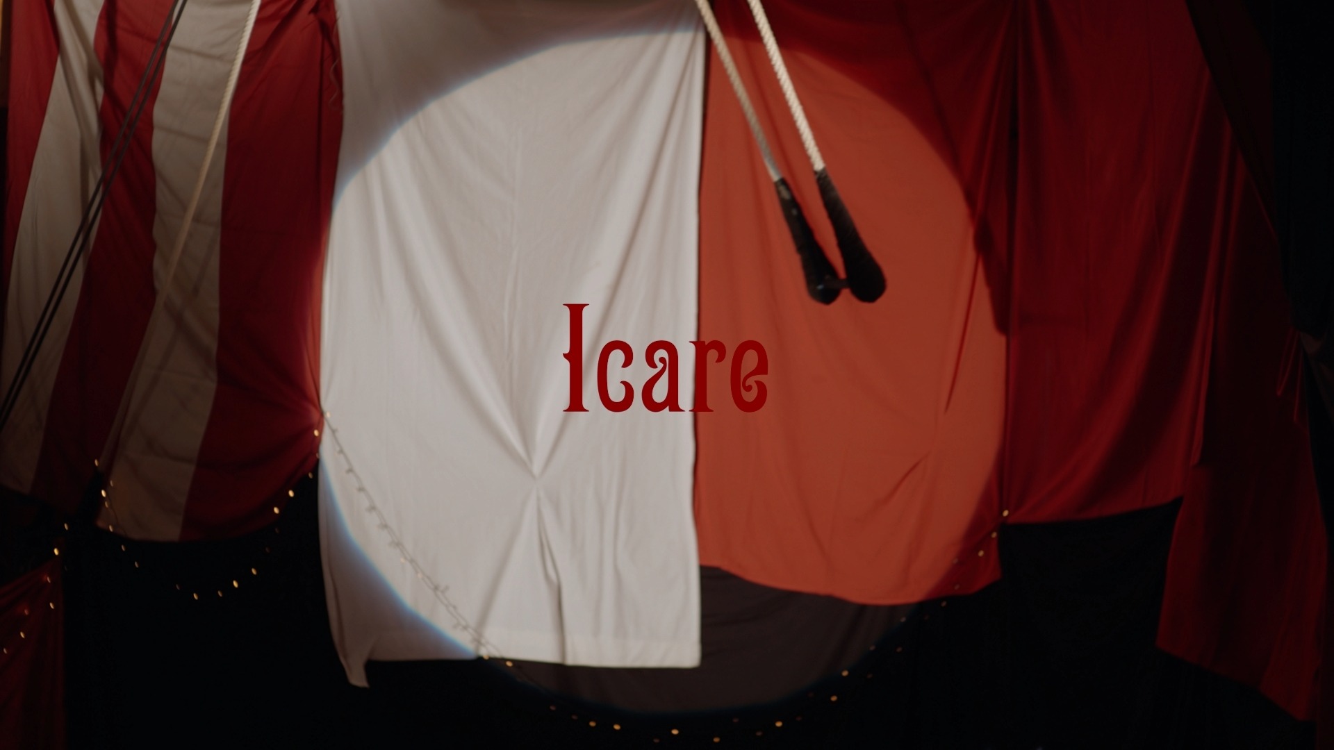 Titre du projet Icare inscrit sur un rideau rouge et blanc décoré de cordes et lumières.